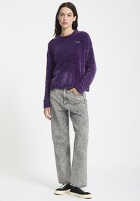 Lilla strikket trøje med rund hals, parret med grå vidde jeans og sorte sneakers med hvide såler.