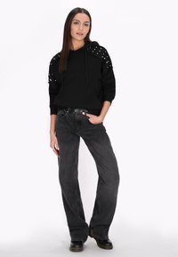 Felpa nera con spalline borchiate, abbinata a jeans neri larghi. Presenta un design semplice e una cintura con dettagli in metallo circolare.