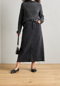 Personne portant un pull en maille gris foncé, ceinture noire, jupe midi en denim noir à ourlet effiloché, ballerines noires avec boucle, tenant un petit sac à main noir.