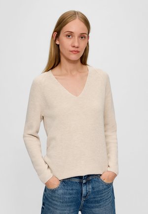 Beige gebreide trui met een V-hals, lange mouwen en een relaxte pasvorm. Gedragen over vervaagde spijkerbroeken in blauw, met een gestructureerde stof.