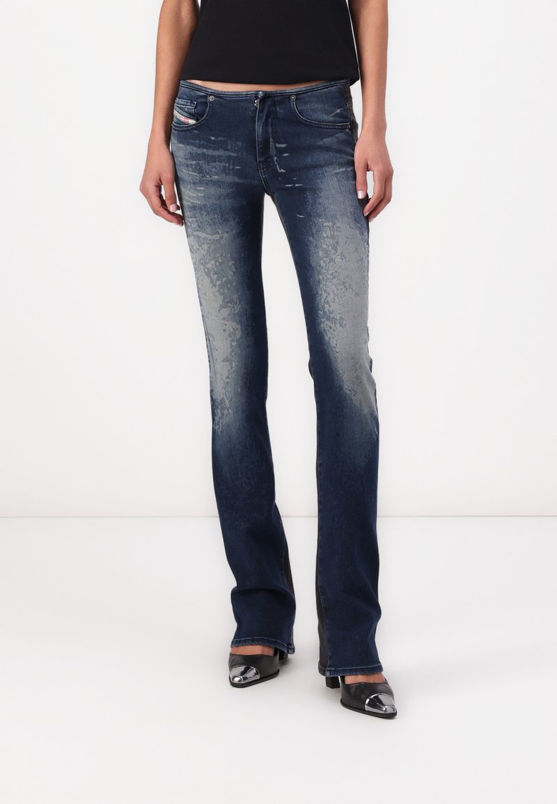Jeans de tiro alto de color azul oscuro con patrones claros de desgaste y desvanecimiento. Presentan cinco bolsillos y un ajuste ceñido, combinados con zapatos negros de punta.
