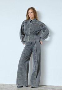 Hallhallane teksajakk nupudega ja kokkusurutud vöökoht, koos laia säärega hallide teksapükstega, millel on külgse seams ja stud aktsendid.