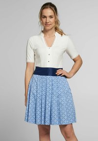 Weißes kurzes Kleid mit kurzen Ärmeln, V-Ausschnitt und Spitzenverzierung, kombiniert mit einem blauen Rock mit floralem Muster und einem breiten marineblauen Taillengummi.