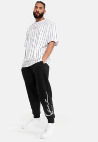 Hvid-og-sort stribet oversized T-shirt parret med sorte joggers med et hvidt grafisk print. Afsluttet med hvide sneakers.