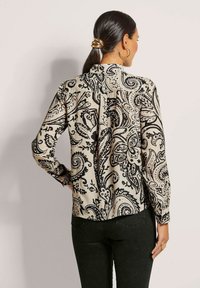 Langärmlige Bluse in Creme mit einem schwarzen Paisleymuster. Mit einem geknöpften Rücken und weichem, strukturiertem Stoff. Abgerundeter Saum.
