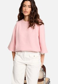 Pull court rose en matériau doux avec des épaules tombantes et des poignets roulés, assorti à un pantalon blanc taille haute.