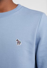 Felpa azzurra chiara con scollatura tonda, polsini a costine e un ricamo colorato di zebra sul petto. Materiale in morbido cotone misto.