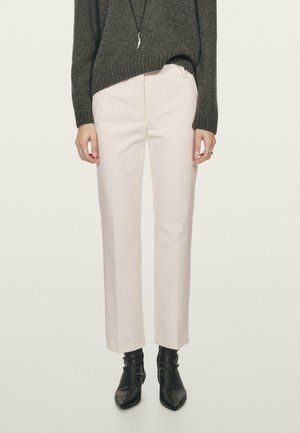 Eine Person trägt hellbeige gerade geschnittene Hosen mit schwarzen spitzen Ankle Boots und einem dunkelgrauen, taillierten Pullover.