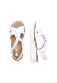 White sandals with cross straps, cork insole, and rubber sole. Features a textured white outsole and cutouts on the side straps.