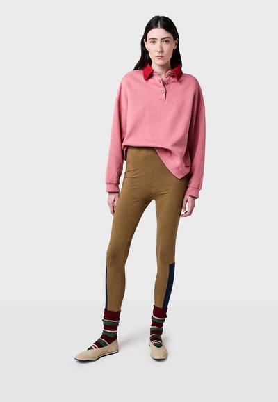 Rosa sweatshirt med röd krage och tre knappar, kombinerad med bruna leggings som har marinblå sidostrecker. Bärs med randiga strumpor och slip-on skor.
