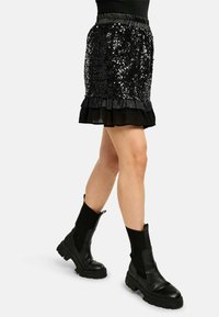 Črna minikratka krilo iz bleščic z nabranim robom, z elastičnim pasom. Kombinirano s črnimi gležnarji in izrazitimi rebrastimi nogavicami.