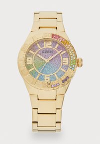 Montre dorée avec un cadran rond, un cadran à paillettes dégradées dans des couleurs pastel et des accents en pierres précieuses autour de la lunette. Bracelets en métal de style bande.
