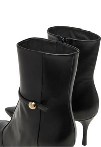 Stivaletti neri in pelle liscia, con cerniera laterale, tacco a spillo sottile e un dettaglio dorato vicino alla caviglia.