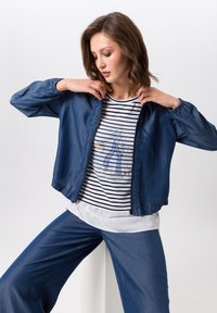 Denim jacket met een ritssluiting, lange mouwen en ribgebreide manchetten. Gecombineerd met een gestreept T-shirt met een grafische print en losse blauwe broeken.