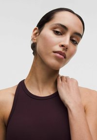 Burgundowy bezrękawnik z wysokim kołnierzem, gładką fakturą, dopasowanym krojem i minimalnymi detalami szwów, podkreślającym ramię i szyję.