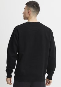 Sudadera negra con un corte relajado, puños acanalados y dobladillo. La parte posterior presenta un sencillo escote circular y una textura de tela suave y lisa.