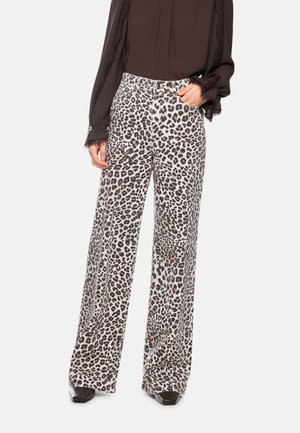Woman wearing high-waist wide-leg pants with black and brown leopard print paired with a dark brown blouse with lace cuffs.