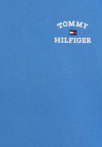 Modré bavlněné tričko s bílým vyšívaným textem "TOMMY HILFIGER" a malým vlajkovým logem. Hladká textura, casual design, krátké rukávy.