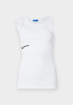 Hvid ribbet tanktop med asymmetrisk design, der har en skulderrem og et subtilt logo i sort på forsiden.
