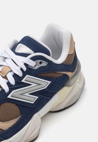 Tenis cu partea superioară din suede și plasă de culoare bleumarin, cu accente bej, șireturi albe și un logo gri. Dispune de o talpă cu amortizare și un material texturat pentru susținere.