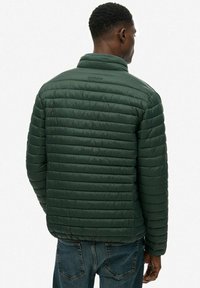 Pikowana kurtka w ciemnozielonym kolorze, z kołnierzem stoj�ącym. Materiał wydaje się gładki z delikatnym połyskiem.