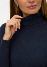 Tumši jūras zila turtlenecks džemperis mīkstā adījumā. Iezīmes ribotas piedurknes un apkakle, ar roku, kas maigi skar apkakli. Redzams sudraba auss gredzens.