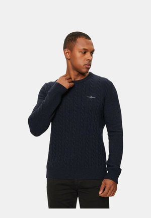 Maglione blu navy a trecce, realizzato in filato spesso, con scollatura rotonda e polsini a coste, dotato di un piccolo logo ricamato sul petto.
