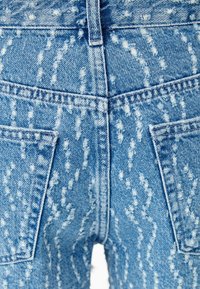 Světle modré džíny z denimu s texturovaným vzorem bílých skvrn. Obsahují dvě zadní kapsy a viditelné švy podél švů.