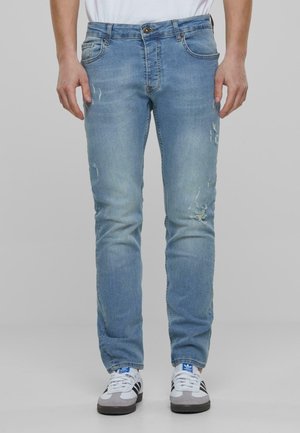 Világoskék farmernadrág, slim fit szabással, kopott részletekkel és varrással. Hagyományos öt zsebes dizájnja van és övhurkokkal rendelkezik.
