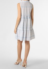 Lichtblauwe mouwloze jurk met complexe patronen, uitlopende zoom en gestructureerde stof. Gecombineerd met beige hakken.