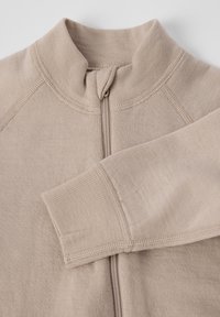 Beige, ritsjack met hoge kraag, gestructureerde brei stof en zichtbare stiksels langs de naden en de rits.