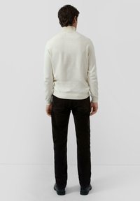 Light cream pullover with a high neck, made of knit fabric. Paired with dark brown corduroy pants, featuring a smooth texture.