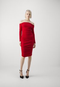 Rochie roșie off-the-shoulder, cu mâneci lungi, textură cu pliuri și siluetă ajustată, purtată cu tocuri stiletto negre.
