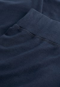 Tkanina od pamuka u tamnoplavoj boji s mekom teksturom, s elastičnim pojasom i detaljima flatlock šivanja. Pogledu blizu pregiba materijala.