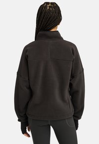 Pullover in pile nero con colletto alto, spalle scese e maniche lunghe. Materiale testurizzato con design pulito, taglio a lunghezza media.