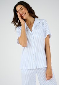 Conjunto de pijama a rayas en azul claro y blanco. Camiseta de manga corta con cuello y bolsillo frontal, combinada con pantalones a juego. Textura de tela suave.