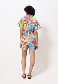 Farbiger, gemusterter Kurz-Jumpsuit mit kurzen Ärmeln, der florale und abstrakte Designs in Orange, Rot, Blau und Grün auf einem hellen Hintergrund zeigt.