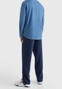 Jeansblå skjorta med lång ärm, avslappnad passform, med knäppningar vid ärmsluten; kombinerad med marinblå sweatpants med en logotyp och vita sneakers med detaljer.