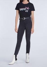 Camiseta negra con gráfico multicolor "DREAM ON", combinada con jeans negro de cintura alta y botas blancas de tacón puntiagudo.