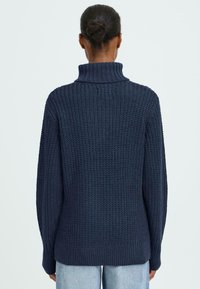 Maglione lavorato a maglia blu navy con colletto alto, caratterizzato da un motivo testurizzato e orlo e polsini a coste, visto da dietro.