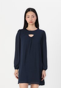 Vestido azul-marinho com mangas bufantes longas, decote redondo e recorte em forma de olho-chave. Feito de tecido leve com uma textura sutil.