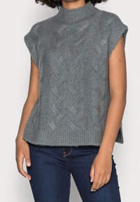 Valokauluksellinen, lyhythihainen pusero vaaleanharmaana, jossa on letitetty neulekuvio ja resorit helmassa. Pehmeä, teksturoitu lanka hienostuneilla yksityiskohdilla.