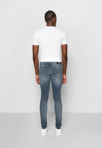Sittande blå denimjeans med en något blekt tvätt, fem fickor och en vit t-shirt. Skorna är vita med en subtil logotyp.