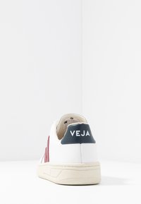 Bílé kožené tenisky s červenými a námořnickými akcenty. Mají texturovanou zadní část s brandingem "VEJA" a krémovou gumovou podrážkou.
