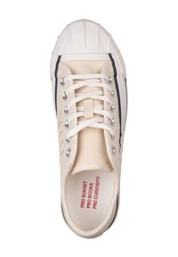 Baskets en toile beige avec bout en caoutchouc blanc, œillets en argent, lacets blancs et accent bleu marine sur le côté extérieur. Le texte à l'intérieur dit "PRO SUNSET PRO BOOKS PRO CURIOSITY."