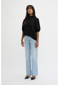 Haut noir à manches courtes avec un col montant, associé à un jean large bleu clair et des chaussures à talons noires à bout pointu. Textures lisses tout au long.
