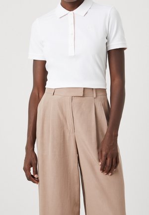 Weißes Polohemd mit Kragen, kurzen Ärmeln und dezentem rosa Akzent. Kombiniert mit hoch taillierten, beigen Hosen. Minimalistisches Design.