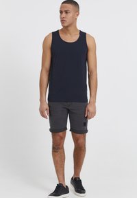 Marine tank topp, grå denimshorts med oppbrettede ermer, og svarte joggesko. Modellen poserer stående, iført avslappet sommerantrekk.