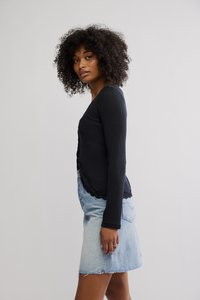 Crni kardigan s dugim rukavima od rebrastog platna s čipkastim rubom, uparen sa svijetlom traper mini suknjom s poderanim rubovima i detaljima stražnjeg džepa.