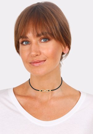 Schwarze Choker-Halskette mit goldener Unendlichkeitssymbol-Mittelstück und kleinen goldenen Akzenten, auf einem hellen Hintergrund präsentiert.